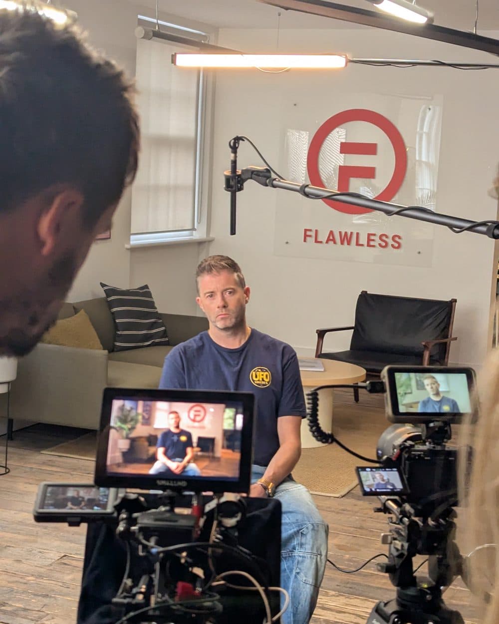 Alex Ford being filmed on a small studio set in front of a Flawless logo